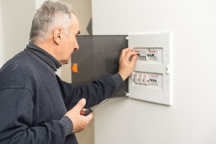Mature male electrician turning off circuit breaker in electrical panel.